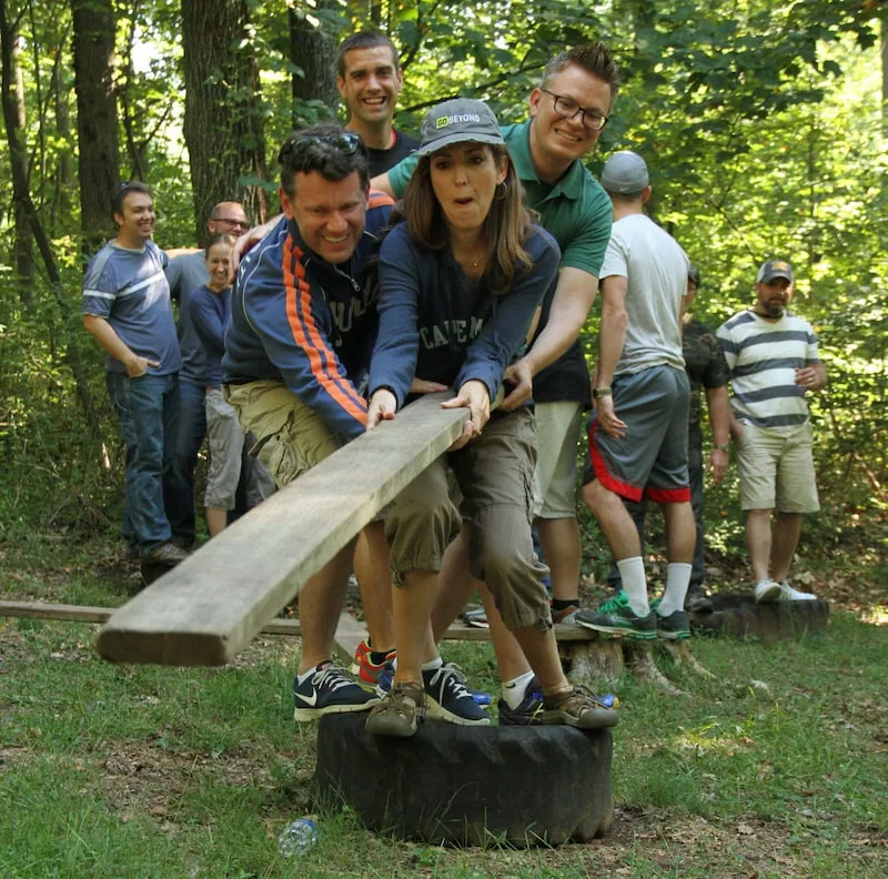 A Group Of Adults Balancing On A Rubber Tire Together