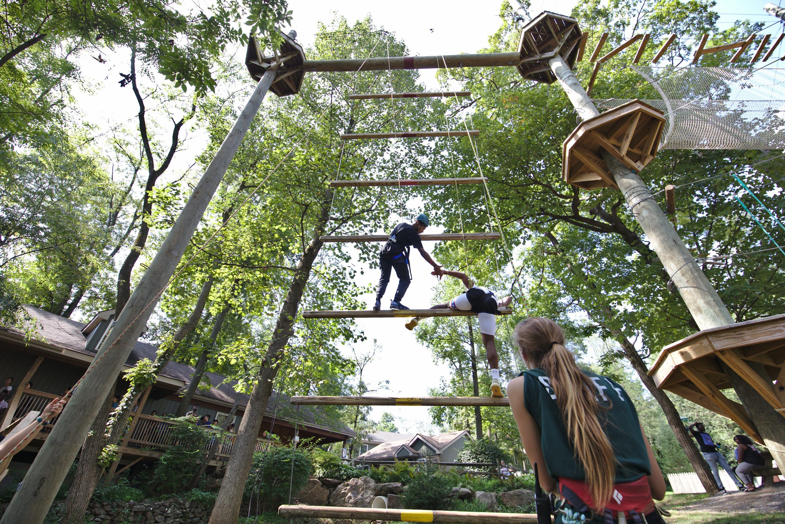 A Friend Giving Another A Helping Hand To Ascend A Large Ropes Obstacle Course